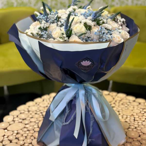 Bouquet of white roses and blue flowers wrapped in navy and white paper