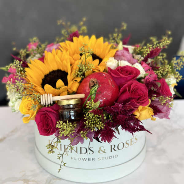 Bouquet with sunflowers, red roses, and a pomegranate in a round box