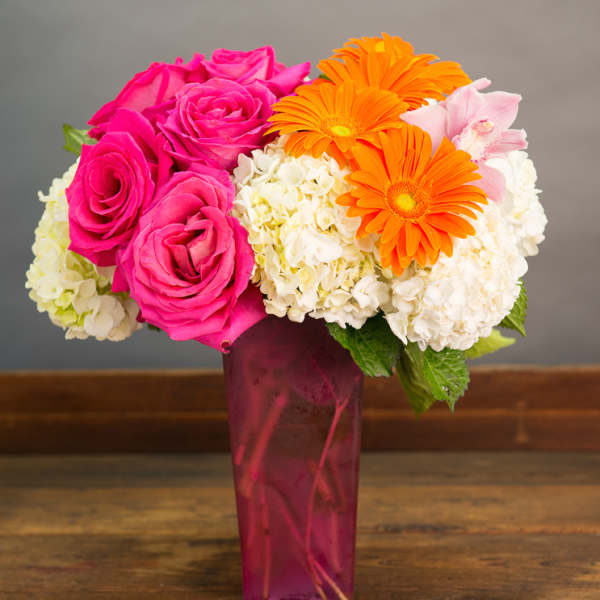 Pink roses and orange gerbera daisies in a tall magenta vase