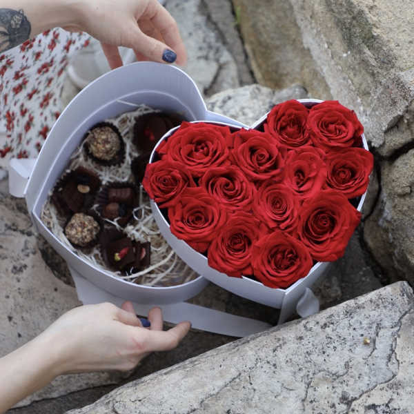Heart-shaped box of red roses beside a box of chocolates