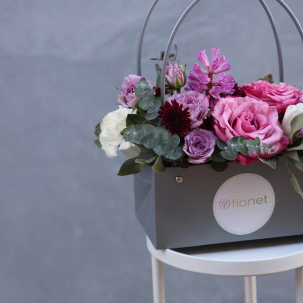 Pink and purple flowers arranged in a gray gift box with handles