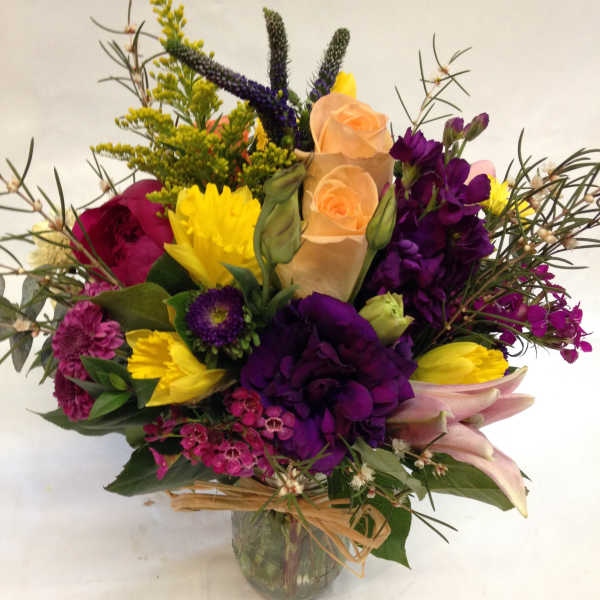 Mixed bouquet of purple, yellow, and peach flowers in a glass vase