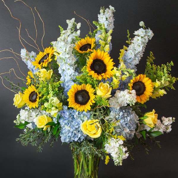 Sunflowers, blue hydrangeas, and yellow roses in a glass vase