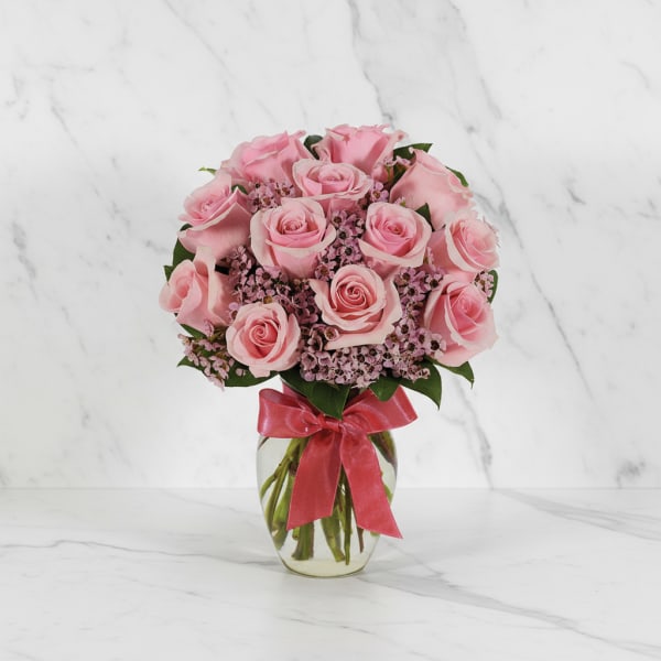 Pink rose bouquet in a clear glass vase with a red ribbon