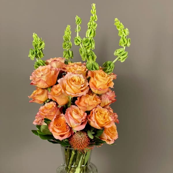 Orange roses in a clear glass vase with tall green spikes