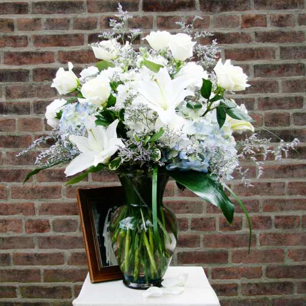White lilies and roses in a glass vase with pale blue hydrangeas