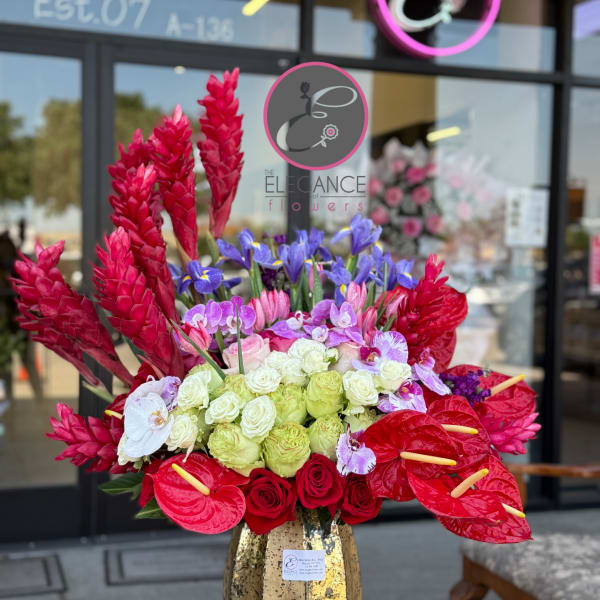 Bright tropical bouquet with red anthuriums, roses, and purple orchids in a gold vase