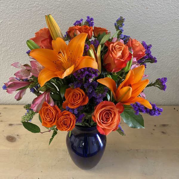 Orange lilies and roses in a blue vase with purple filler flowers