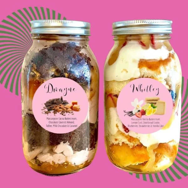 Two dessert jars with layered cake and frosting on a pink background
