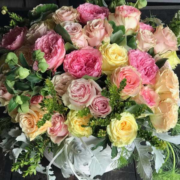 Bouquet of pink, peach, and yellow roses with greenery in a white container