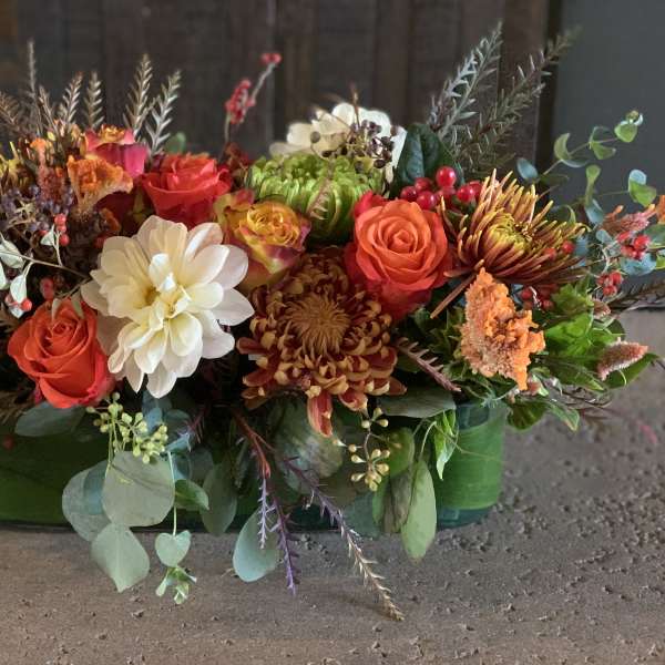 Mixed floral arrangement with roses, chrysanthemums, and white dahlias in a green container