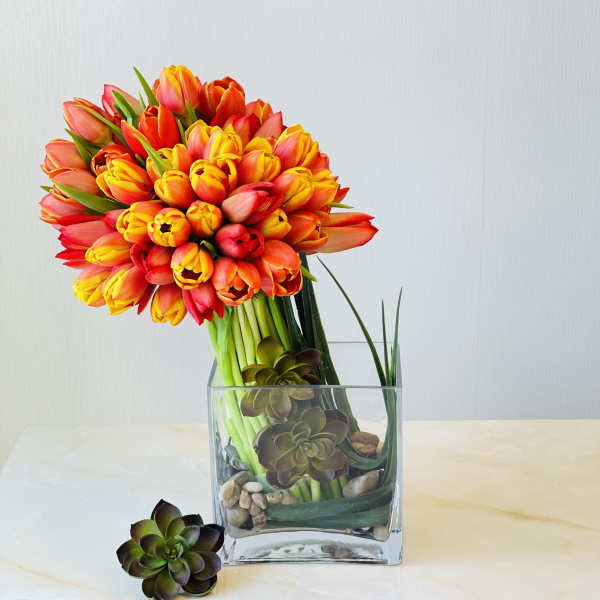 Bouquet of orange and yellow tulips in a clear square vase