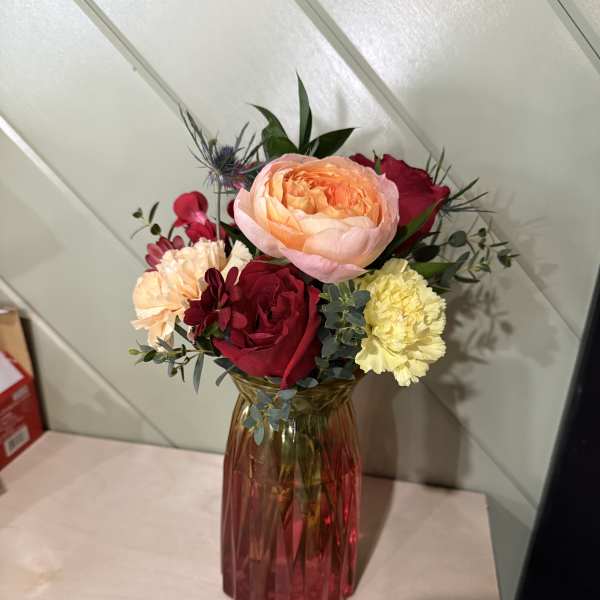 Mixed bouquet of roses and carnations in a red glass vase