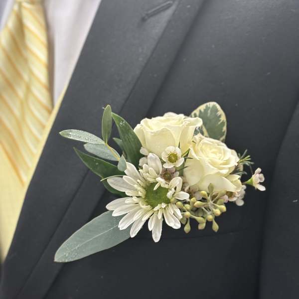 White boutonniere with roses and daisies on a dark suit lapel