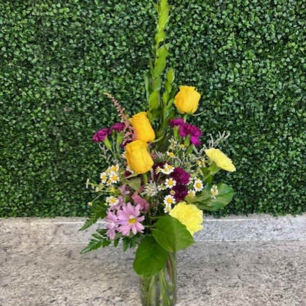 Mixed bouquet in a clear glass vase with yellow roses and purple flowers
