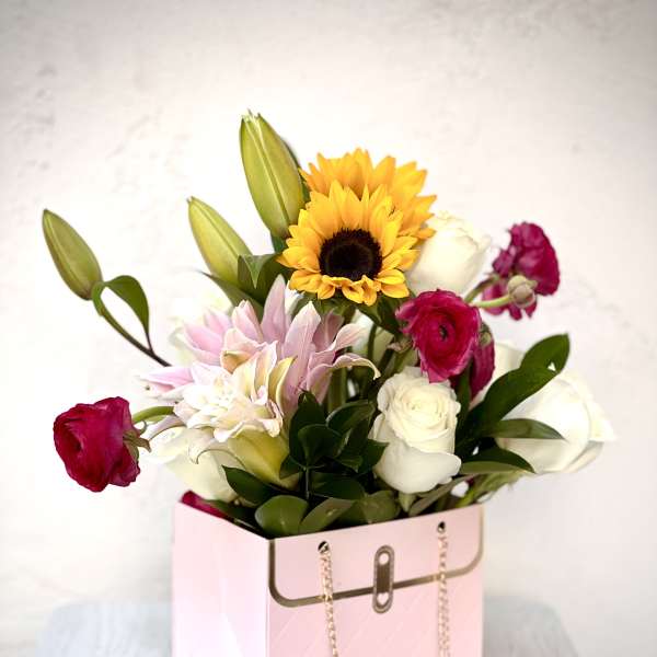 Mixed bouquet in a pink gift box with sunflowers, roses, lilies, and ranunculus