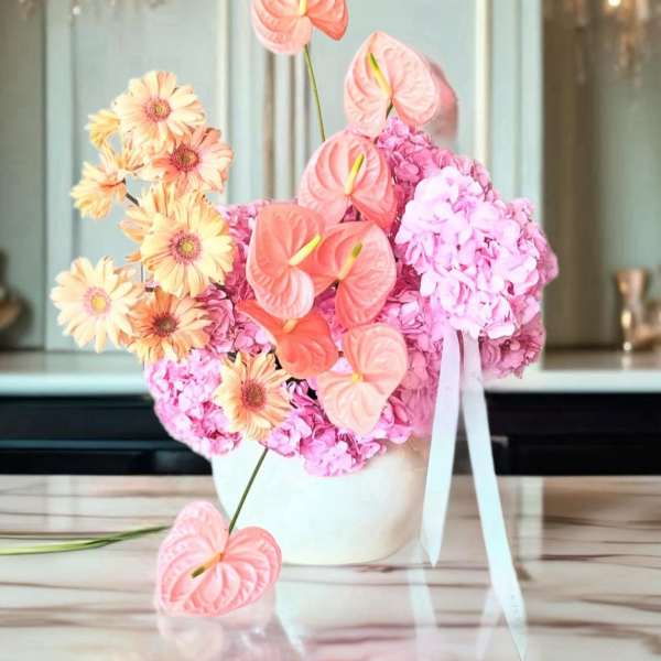 Pink and peach floral arrangement in a white vase with ribbon