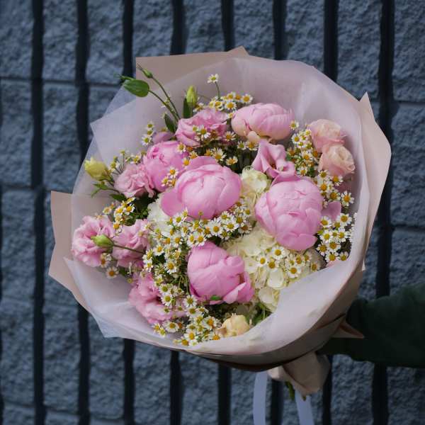 Pink bouquet with white daisy-like flowers wrapped in pale paper