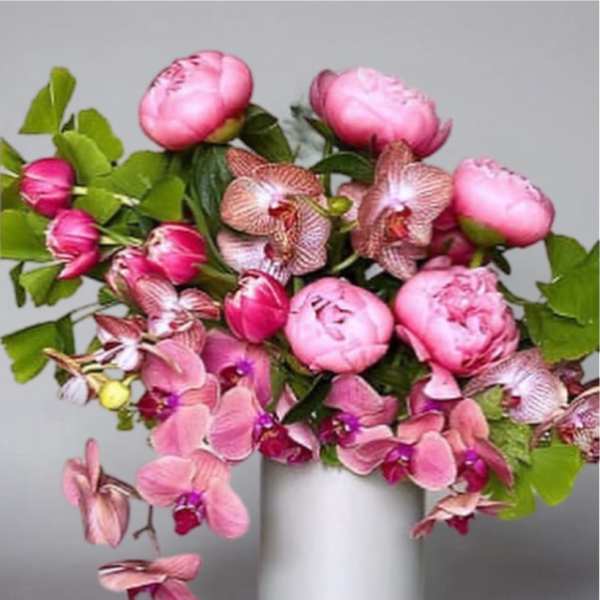 Pink peonies and orchids arranged in a white vase