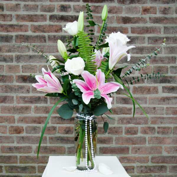 Pink and white lilies arranged in a glass vase with trailing beads
