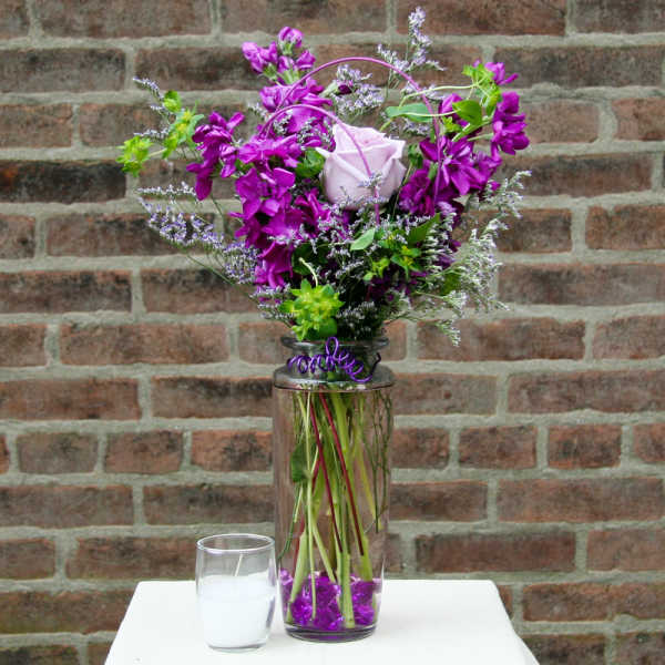 Purple floral arrangement in a tall glass vase with a white rose