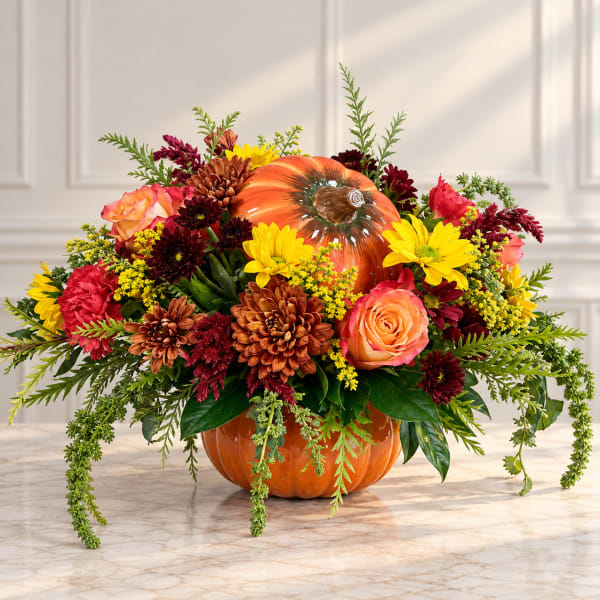 Fall floral arrangement in a pumpkin-shaped container with roses and mums