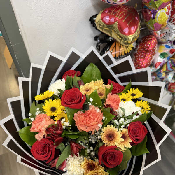 Mixed bouquet of red roses, yellow daisies, and carnations in black wrap