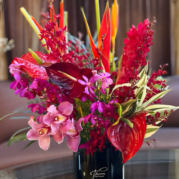 Tropical flower arrangement in a black vase with pink and red blooms