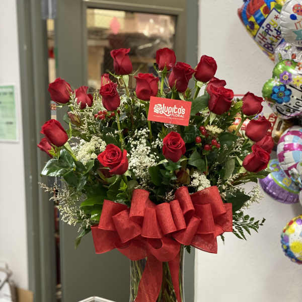 Red roses arranged in a clear glass vase with a large red bow