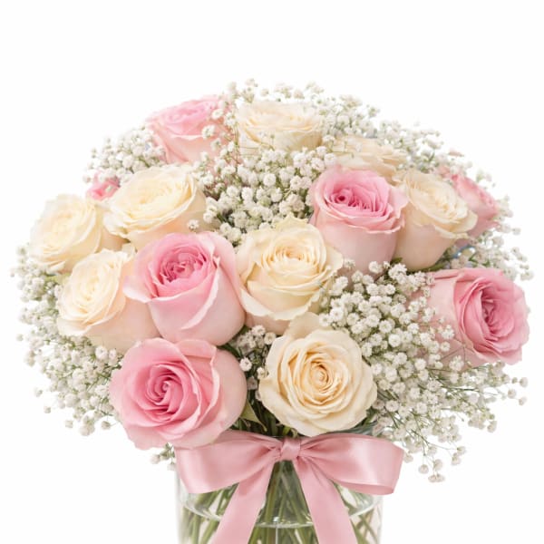 Pink and cream roses in a glass vase with a pink ribbon