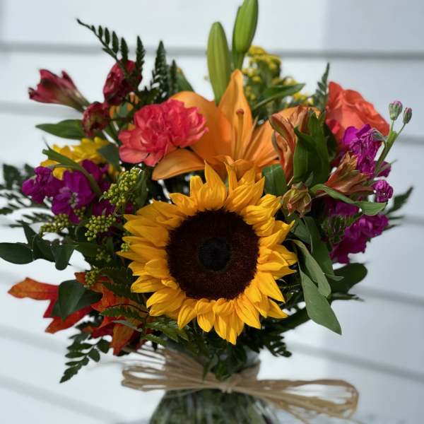 Mixed bouquet with a sunflower, orange lily, and pink flowers in a glass vase