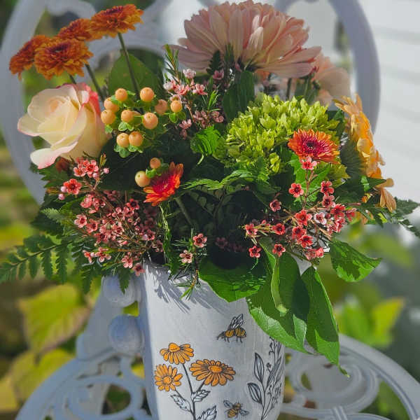 Mixed bouquet in a painted white mug with orange and pink flowers.