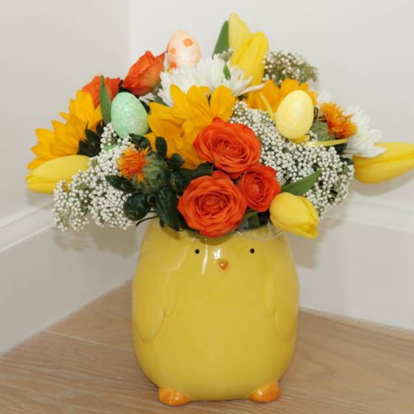 Yellow chick-shaped vase holding a bright mixed flower arrangement