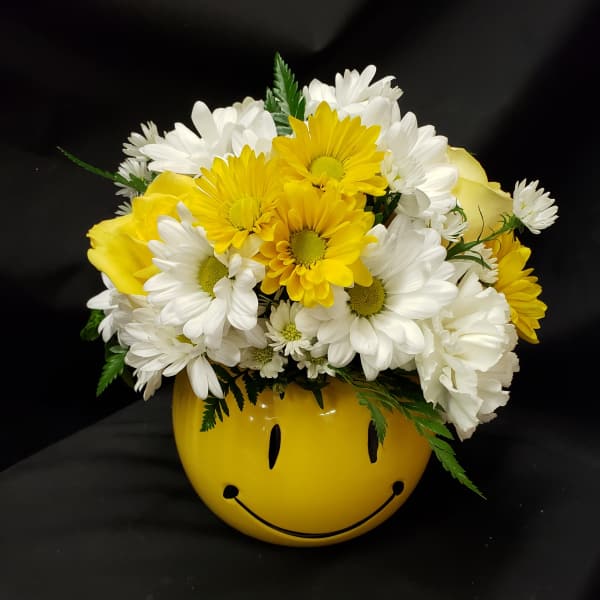 Yellow and white daisy bouquet in a smiley-face vase