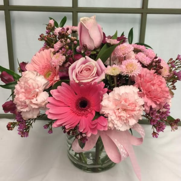 Pink mixed flower bouquet in a clear glass vase with a ribbon