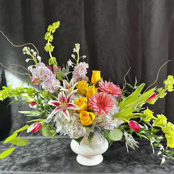 Colorful mixed flower arrangement in a white vase with long branching accents