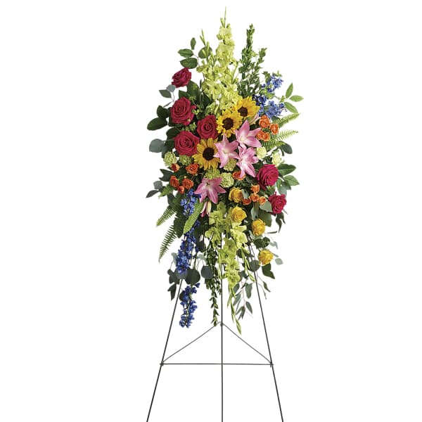 Tall standing floral spray with roses, lilies, sunflowers, and blue flowers on an easel