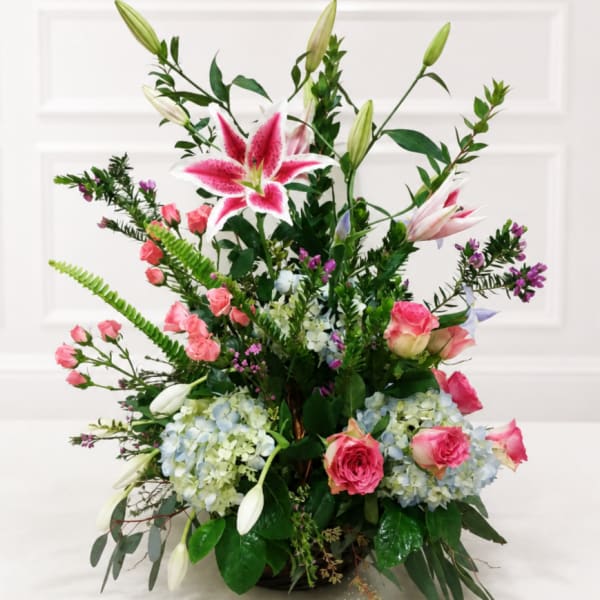 Tall floral arrangement with pink lilies, pink roses, and blue hydrangeas in a vase