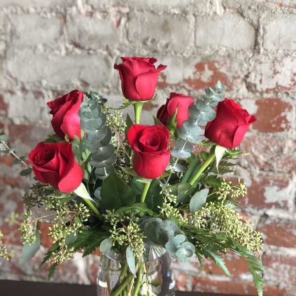 Red roses arranged in a clear glass vase with eucalyptus