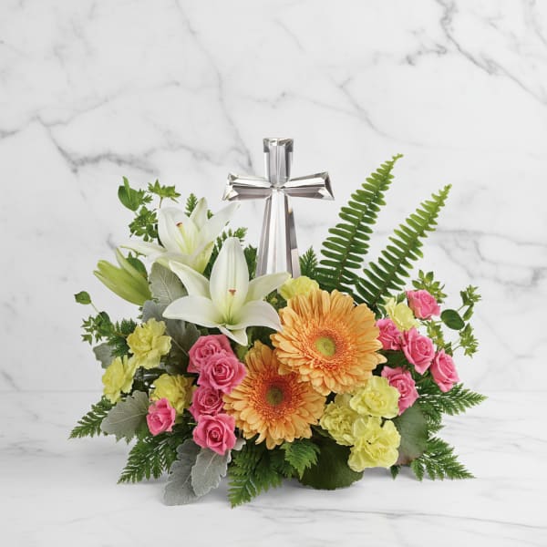 Floral arrangement with white lilies, pink roses, orange gerberas, and a silver cross