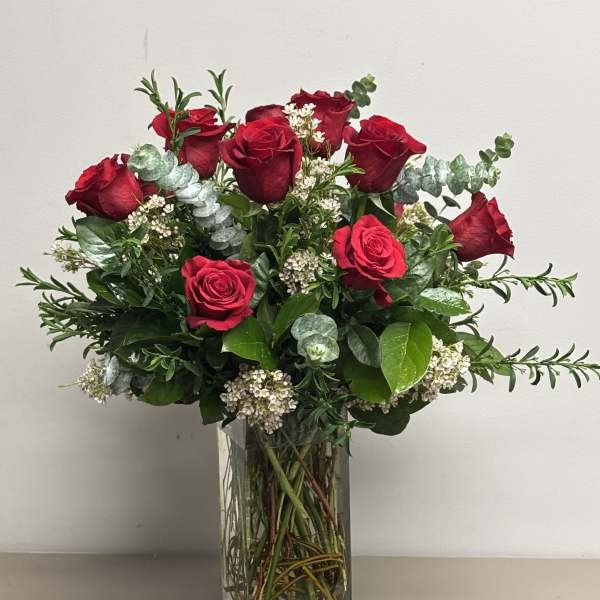 Tall arrangement of red roses with white filler flowers in a clear rectangular glass vase