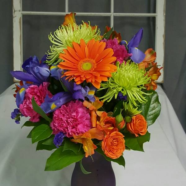 Colorful mixed bouquet in a dark vase with orange, purple, pink, and green blooms