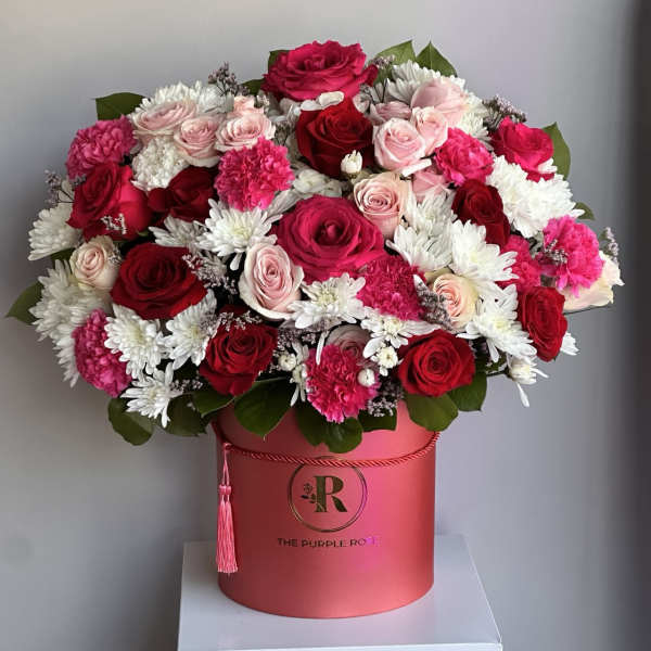 Round hat box of red, hot pink, and pale pink roses with white mums and pink carnations