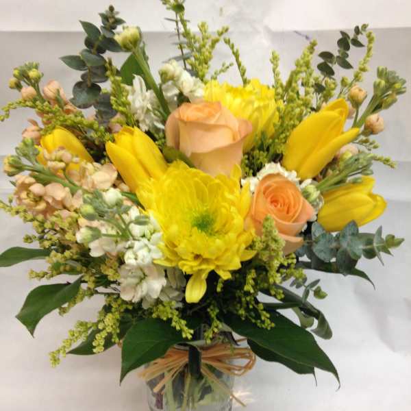 Yellow and peach flower arrangement with roses and tulips in a clear glass jar tied with raffia