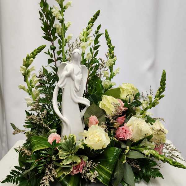 White angel figurine surrounded by cream and pink roses in a floral arrangement