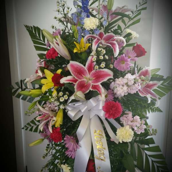 Tall mixed flower standing spray with lilies, roses, and a white ribbon