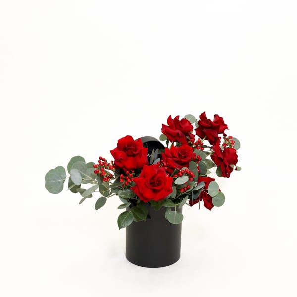 Red roses arranged in a black cylindrical vase with eucalyptus and berry accents