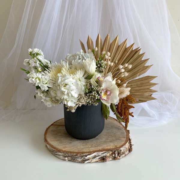 White floral arrangement in a black vase with a gold fan backdrop