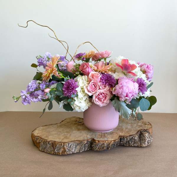 Pink and purple floral arrangement in a ribbed vase on a wood slab