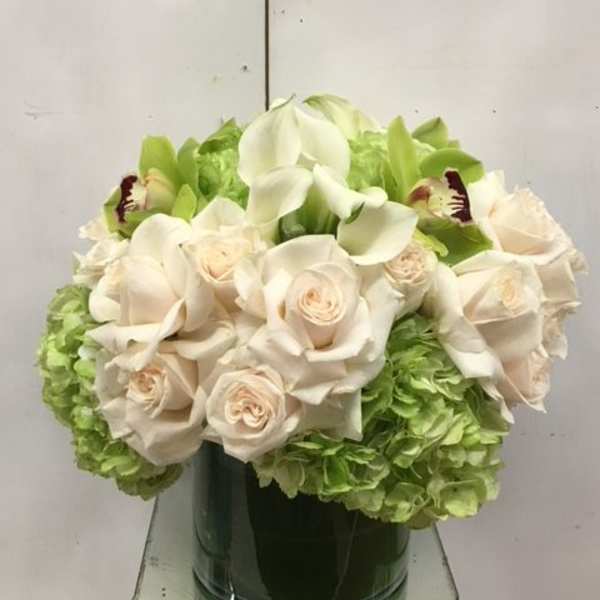 White roses and calla lilies arranged with green hydrangeas in a glass vase